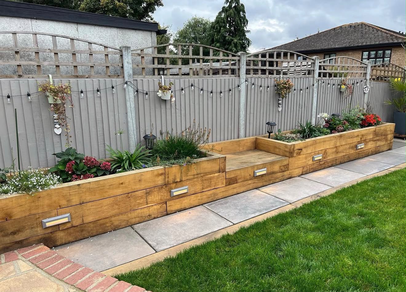 Tiered oak sleeper raised planters with porcelain paving and step lighting