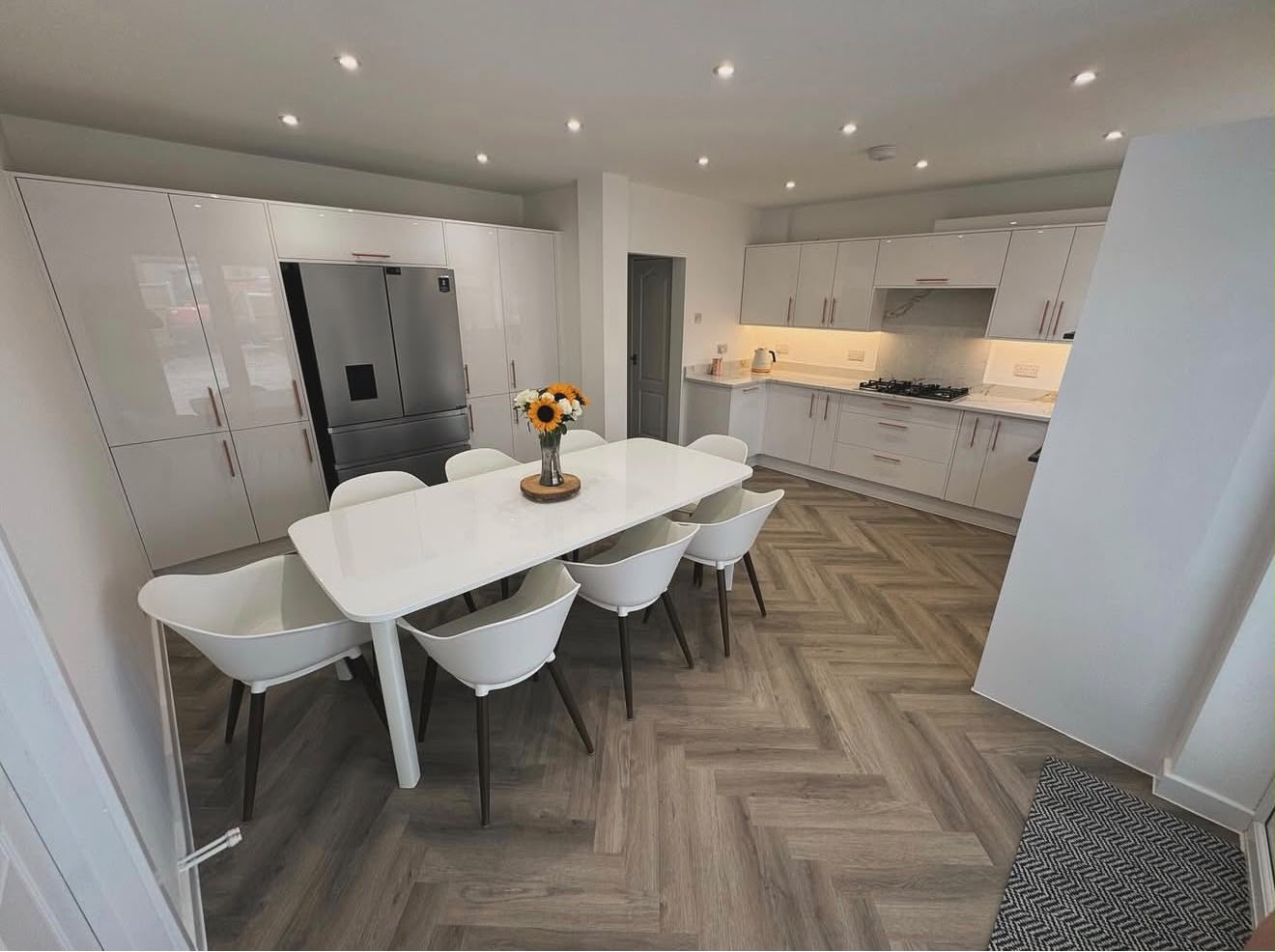 Open-plan kitchen extension with light grey gloss units, integrated American fridge and herringbone flooring