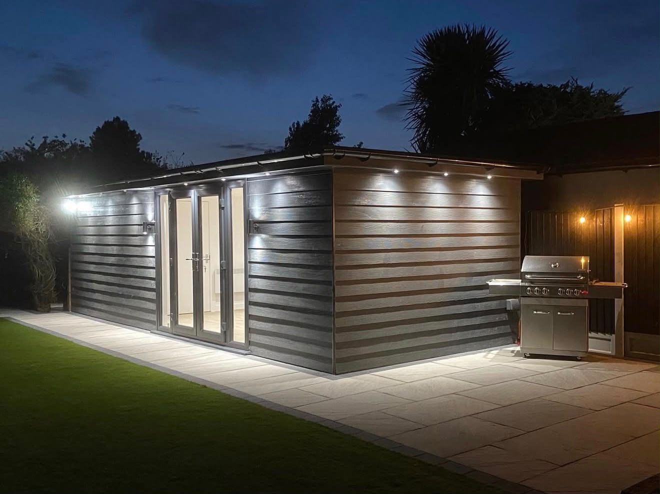 Luxury garden room at night with grey composite cladding and exterior downlights