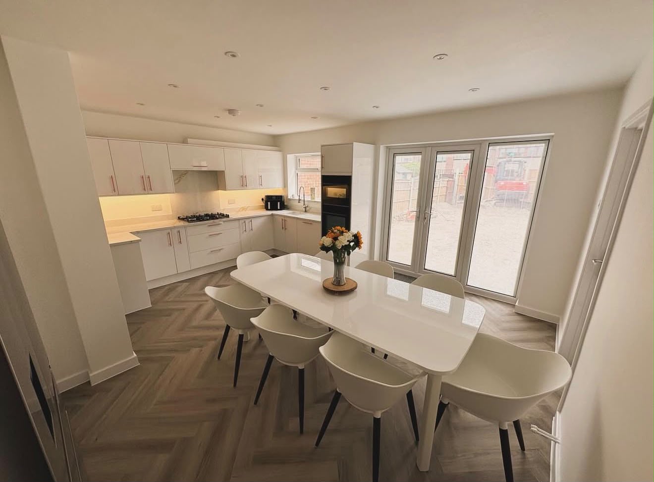 Newly fitted kitchen-diner with white gloss cabinetry, herringbone flooring and French doors to garden