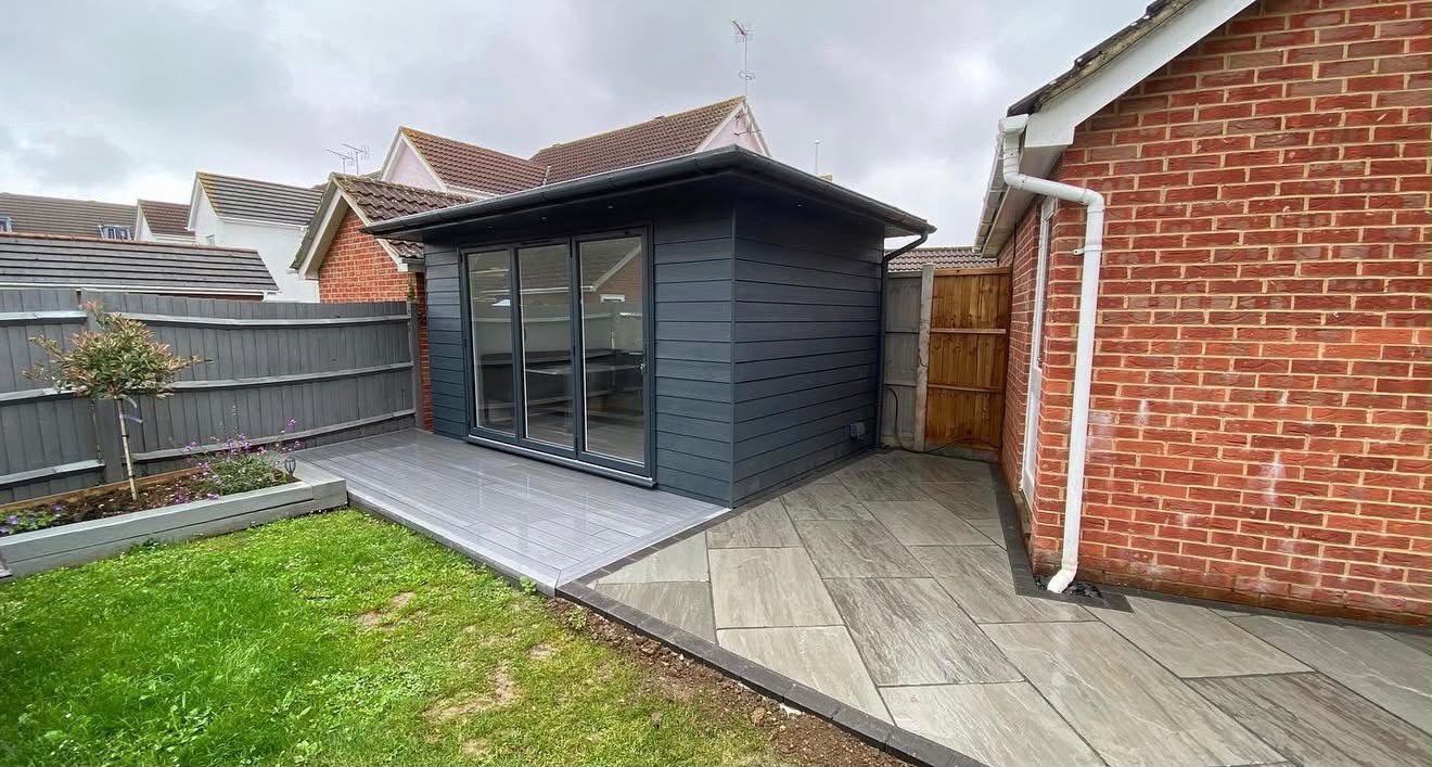 Compact dark grey clad garden office with bifold doors and porcelain patio